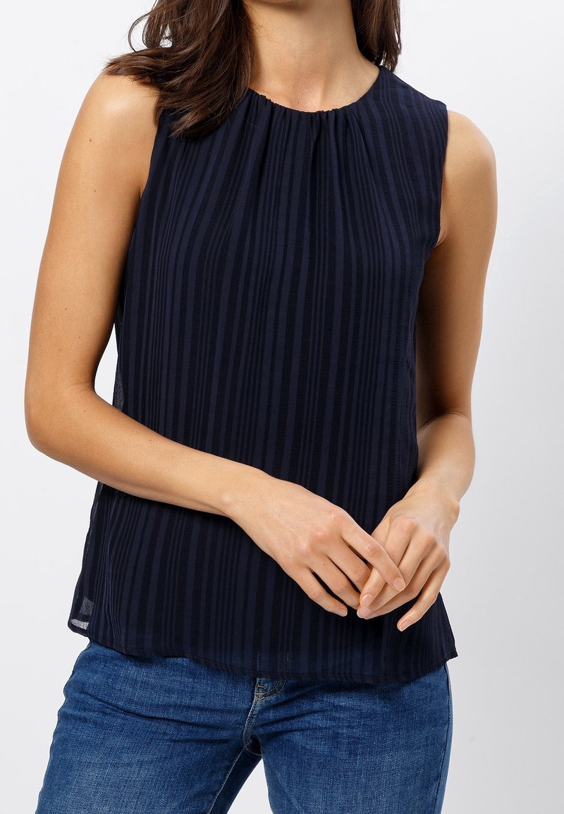 Mörkblå ärmlös topp med vertikala ränder, insamlad hals, mjuk tygkvalitet och avslappnad passform, bärs med denimjeans.