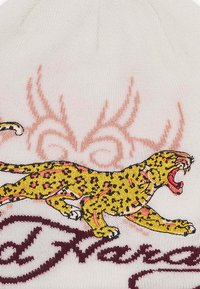 Hvid strikket hue med en broderet gul leopard med sorte pletter, pink accenter og maroon tekst. Baggrunden har et subtilt pink design.