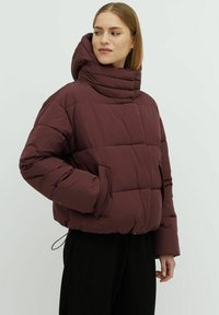 Giacca a piumino borgogna con alto colletto, design trapuntato, tasche laterali e orlo con cordoncino. Tessuto morbido e imbottito con una superficie liscia.