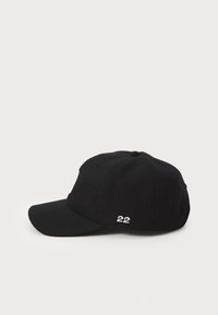Svart baseballcaps i stoff med buet skjerm, med brodert "22" på siden. Seks ventilasjonshull er synlige.