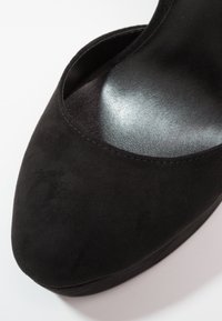 Chaussure pour femme en suède noir à bout pointu avec semelle intérieure noire lisse et brillante, vue en gros plan sous un angle.