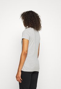 Šedé tričko s krátkým rukávem s přiléhavým střihem a hladkou texturou. Švy na bocích, spárované s tmavými kalhotami.