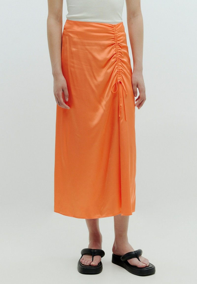 Mid-length oranjesatinrock mit gerafftem Detail und verstellbarem Bindebandverschluss an der Seite. Getragen mit schwarzen Plateausandalen.