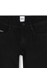 Jeans in denim nero con un classico design a cinque tasche, chiusura con bottone e un'etichetta con "BOSS" sulla vita e sulla tasca posteriore.