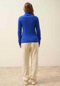 Blauer gerippter Rollkragenpullover mit langen Ärmeln, taillierter Passform, kombiniert mit cremefarbenen, weit geschnittenen Hosen. Glatte Textur und lässiger Stil.