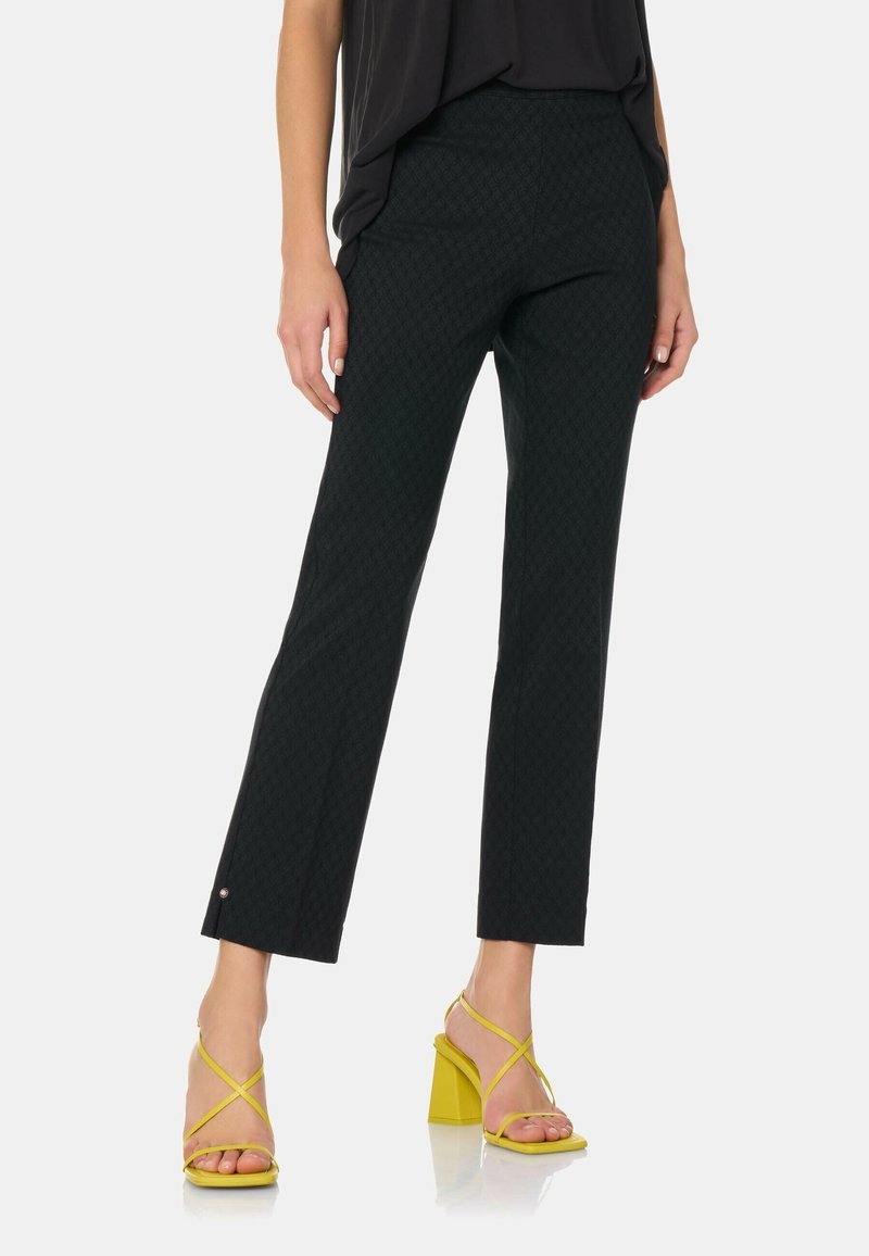 Zwarte broek met een rechte pasvorm en een patroon, voorzien van zij-splits en kleine zilveren hardware accenten, in combinatie met gele haksandalen.