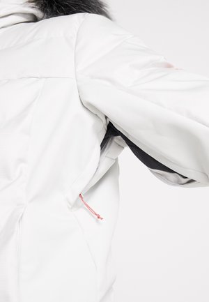 Veste d'hiver blanche avec panneau de ventilation noir sous les aisselles et tirette de fermeture éclair rose, portée par une personne avec capuche bordée de fourrure visible.