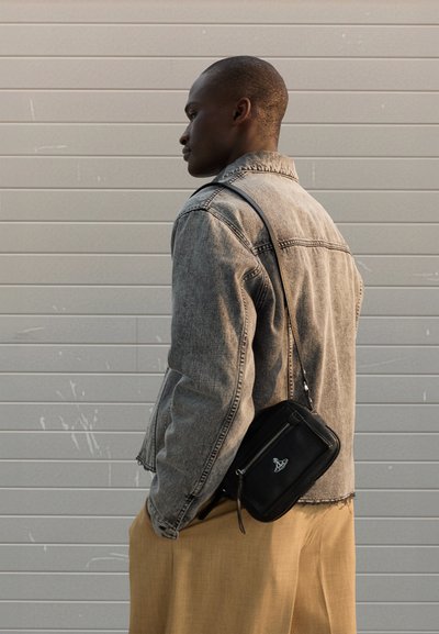 Jeansjacka med fransiga kanter, grå färg. Svart läder axelremsväska med dragkedja och logodetalj. Byxor i neutrala toner, lösa passformen.