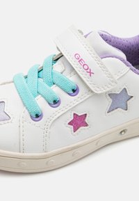 White leather sneaker with turquoise laces and Velcro strap. Features purple and glittery star cutouts and a textured purple tongue.