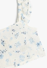 Hvid blomster crop top lavet af letvægtsstof, med blå blomster mønstre, flæset strop og en tekstureret overflade.