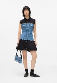 Φόρεμα από τζιν και μαύρο ύφασμα που διαθέτει εφαρμοστό μπλε κορμό με τσέπες και φαρδιά μαύρη φούστα. Συμπληρώνεται με μια μικρή μπλε τσάντα.