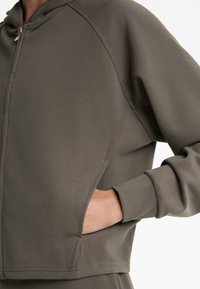 Grau gestreifter Zip-Hoodie mit Kapuze, Seitentaschen und eingelassenen Ärmeln. Glatte Textur mit ausgeprägten Nähten und taillierter Silhouette.