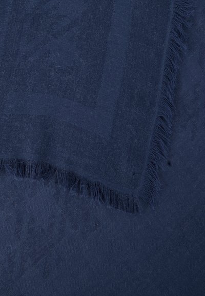 Tissu bleu foncé avec une texture subtilement imprimée et des bords effilochés, plié sur lui-même.