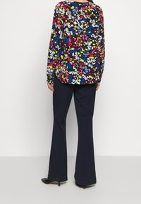 Długo rękawowa bluzka w kwiatowy wzór w jasnych kolorach na czarnym tle, zestawiona z ciemnoniebieskimi spódnicami w dzwony i czarnymi szpilkami.