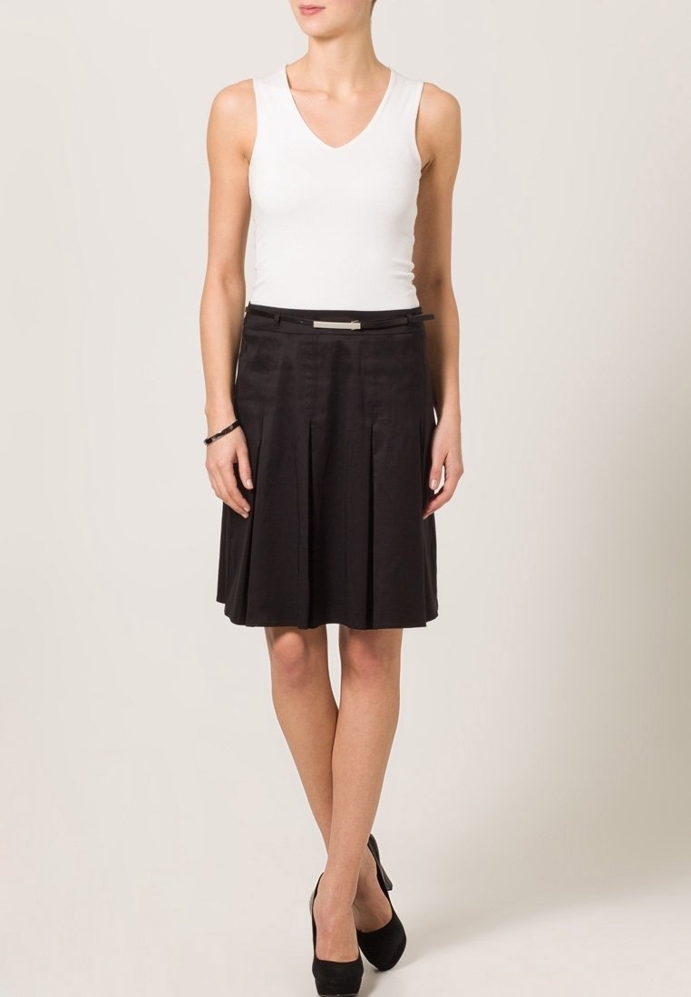 Witte v-hals tanktop en zwarte geplisseerde rok met een zilverkleurige tailleband, gemaakt van gladde stof. Boven de knie lengte.