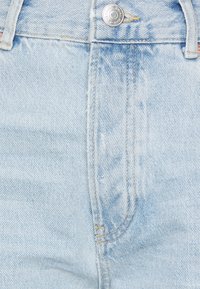 Jeans in denim blu chiaro con chiusura a zip e bottone argentato, con aree sbiadite e dettagli di cucitura visibili.