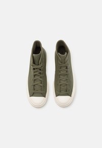 High-top sneakers in olive green synthetic material with matching laces, white rubber toe cap, and textured side panels.