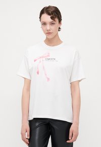Vit bomull t-shirt med korta ärmar, med en rosa bandgrafik och ordet "COQUETTE" i svart text under.