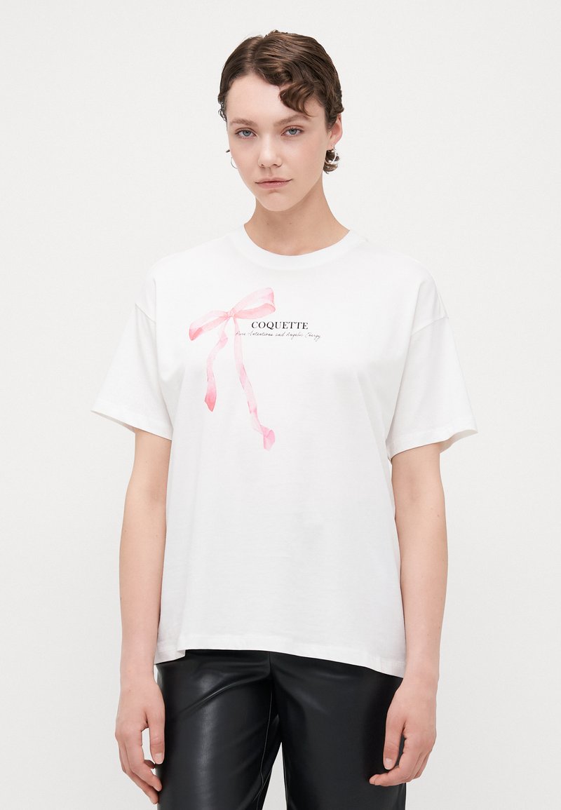 Vit bomull t-shirt med korta ärmar, med en rosa bandgrafik och ordet "COQUETTE" i svart text under.