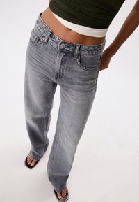 Jean taille haute à jambes larges en denim gris délavé. Comprend cinq poches, une fermeture à boutons et un léger effet froissé le long du tissu.