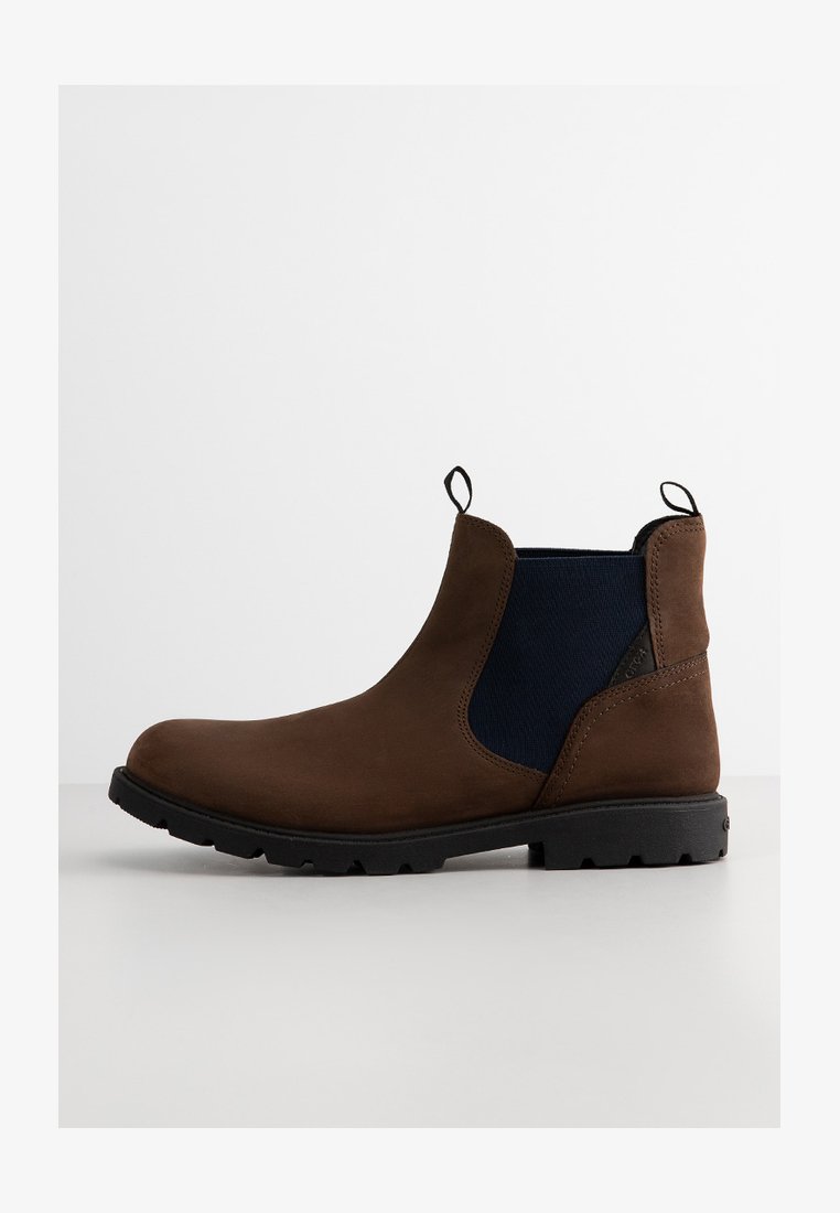 Stivaletto in suede marrone con pannelli laterali elasticizzati blu navy, linguette e suola in gomma testurizzata. Presenta una punta arrotondata e cuciture minime.