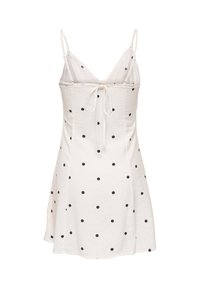 Robe blanche sans manches à pois noirs, fines bretelles réglables et détail noué à l'avant au niveau de la poitrine, jupe légèrement évasée.