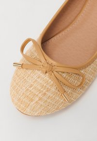 Ballerines en paille tissée avec un nœud en cuir beige clair et des accents dorés ; bout rond et doublure intérieure lisse.