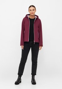Burgundowa kurtka z kapturem, kontrastowa różowa podszewka, zamek błyskawiczny z przodu i dwie boczne kieszenie, w zestawie z czarnymi dżinsami i masywnymi czarnymi butami.