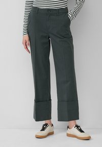 Donkergroene wijdvallende broeken met een gladde textuur, voorzien van een knoopsluiting en opgerolde manchetten, gecombineerd met beige en zwarte sneakers.