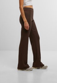 Pantalon évasé en corduroy marron avec une taille haute, fabriqué en matériau extensible, associé à des baskets grises.