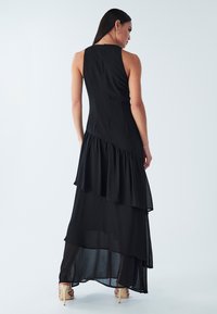 Juoda rankovių neturinti suknelė su sluoksniuota išvaizda, puošta raukiniais apačioje. Minkšta medžiaga, lygi tekstūra ir diskretiška užtrauktuko uždarymo detalė nugaroje.