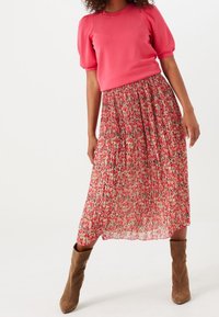 En rosa topp med puffärmar i kombination med en midjelång, plisserad blommig kjol i nyanser av rosa, röd och grön. Bruna, avslappnade ankelboots fulländar looken.