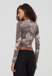 Top corto a manica lunga in un materiale grigio trasparente con una stampa di farfalle. Il design presenta modelli variabili e una silhouette aderente.