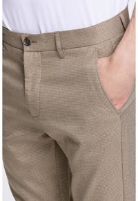 Pantaloni a quadri beige con un tessuto strutturato, dotati di chiusura a bottone e tasche laterali, taglio slim con una finitura liscia.