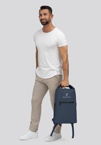 Mochila de color azul marino con una textura suave y lisa, que cuenta con un bolsillo frontal con cremallera y correas de hombro ajustables. Logo exhibido de manera prominente.