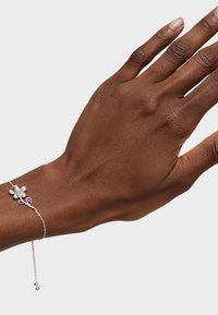Bracciale floreale in argento con un fiore centrale incastonato con un diamante e due pietre a forma di goccia viola su una delicata catena.