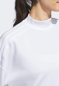 White high-collar athletic top with long sleeves, featuring three contrasting vertical stripes on shoulders, made from smooth, lightweight fabric.
