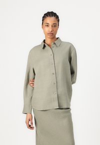 Light green linen shirt with a collared neckline, button front, and long sleeves, paired with a matching light green skirt.