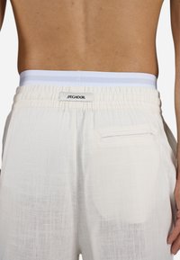 White linen shorts with an elastic waistband featuring light blue stripes. Includes a back pocket and textured fabric finish.