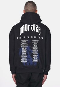 Schwarzer Pullover mit Kapuze und großem Grafikdruck auf dem Rücken. Beinhaltet die Texte "DROP SIZE" und "HUSTLE CULTURE TOUR" sowie aufgelistete Städtenamen.
