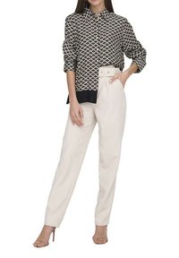 Blouse à motifs noir et blanc avec un col pointu, assortie à un pantalon crème ajusté, doté d'une taille ceinturée et de poches latérales.