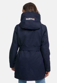 Manteau à capuche bleu marine avec une taille cintrée, fermeture éclair et un col matelassé. Présente un patch logo multicolore sur la capuche.