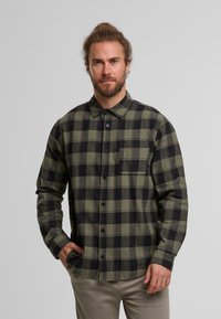 Grünes und schwarzes karierter Flanellhemd mit Knöpfen vorne, langen Ärmeln und einer Brusttasche, präsentiert an einem Mann.