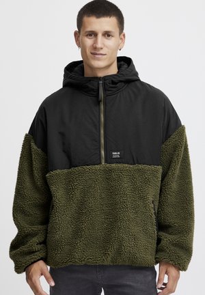 Olive green fleece pullover with black nylon top. Features a hood, half zip closure, and a small brand patch on the chest. Textured fabric.