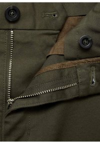 Tissu vert avec une fermeture éclair visible, dents en laiton et boutons noirs. Comprend un ourlet cousu et une doublure marron douce.