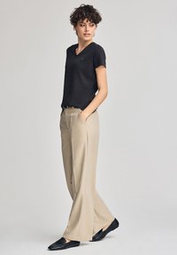 Czarna koszulka V-neck, beżowe spodnie o szerokiej nogawce i czarne mokasyny. Gładki materiał o minimalistycznym designie i luźnym kroju.