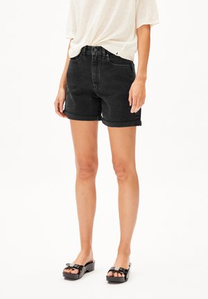 Shorts en denim noir avec une taille haute et des ourlets roulés, dotés de passants de ceinture et d'une fermeture par bouton. Modèle associé à des sandales à plateforme noires.