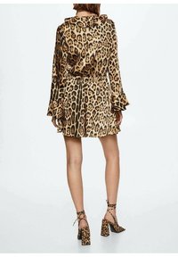 Sukienka w wzór lamparta z długimi rękawami dzwonowymi, wcięciem w talii i zwiewnym dołem. Połączona z wysokimi butami na obcasie w wzór lamparta.