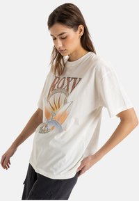 Biała bawełniana koszulka z kolorowym graficznym nadrukiem przedstawiającym elementy słońca i surfingu, z krótkimi rękawami i luźnym krojem.