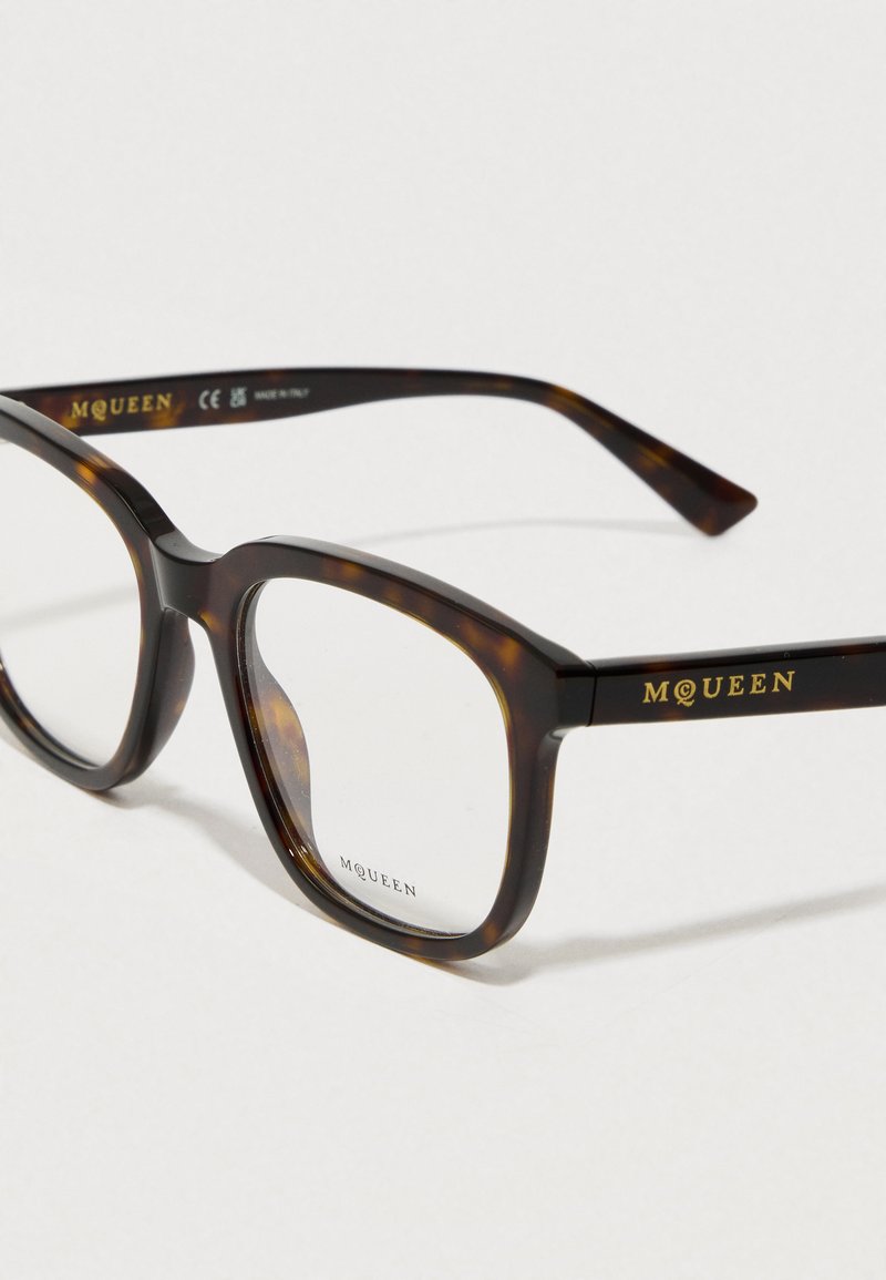 Lunettes écaille de tortue avec une monture carrée, des verres transparents et une inscription dorée sur les branches, ayant une finition polie.